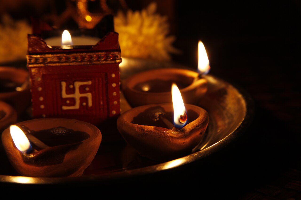 Lit clay diyas on a brass plate beside a small decorated lamp holder