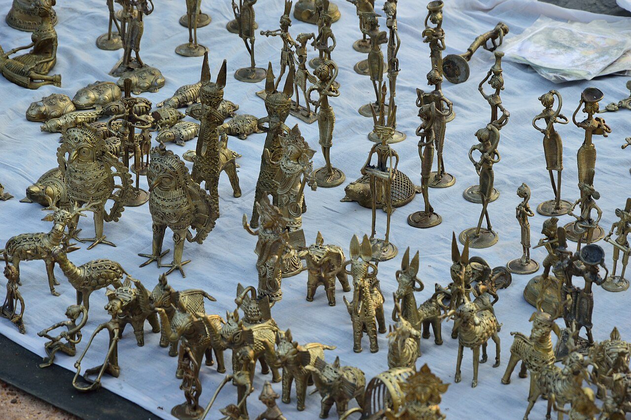 Rows of Dhokra brass figures laid out for sale on a cloth at an open-air weekly market