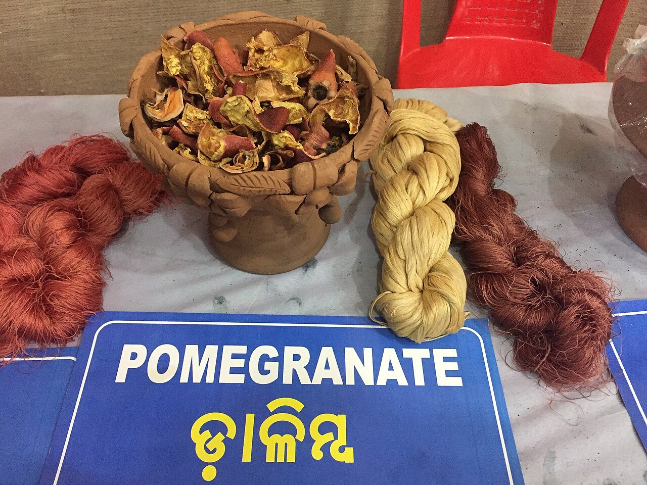 Skeins of tasar silk yarn dyed rust and gold beside a bowl of dried pomegranate rind, with a sign reading Pomegranate