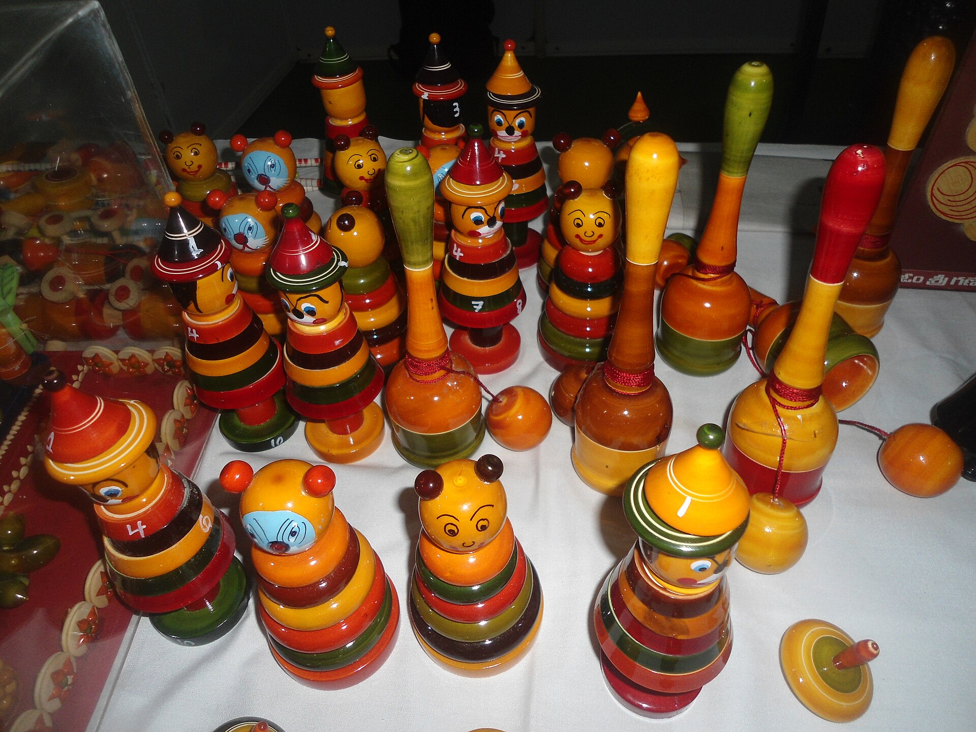 Rounded wooden Etikoppaka toys in yellow, coral and green lacquer colours arranged on a wooden surface