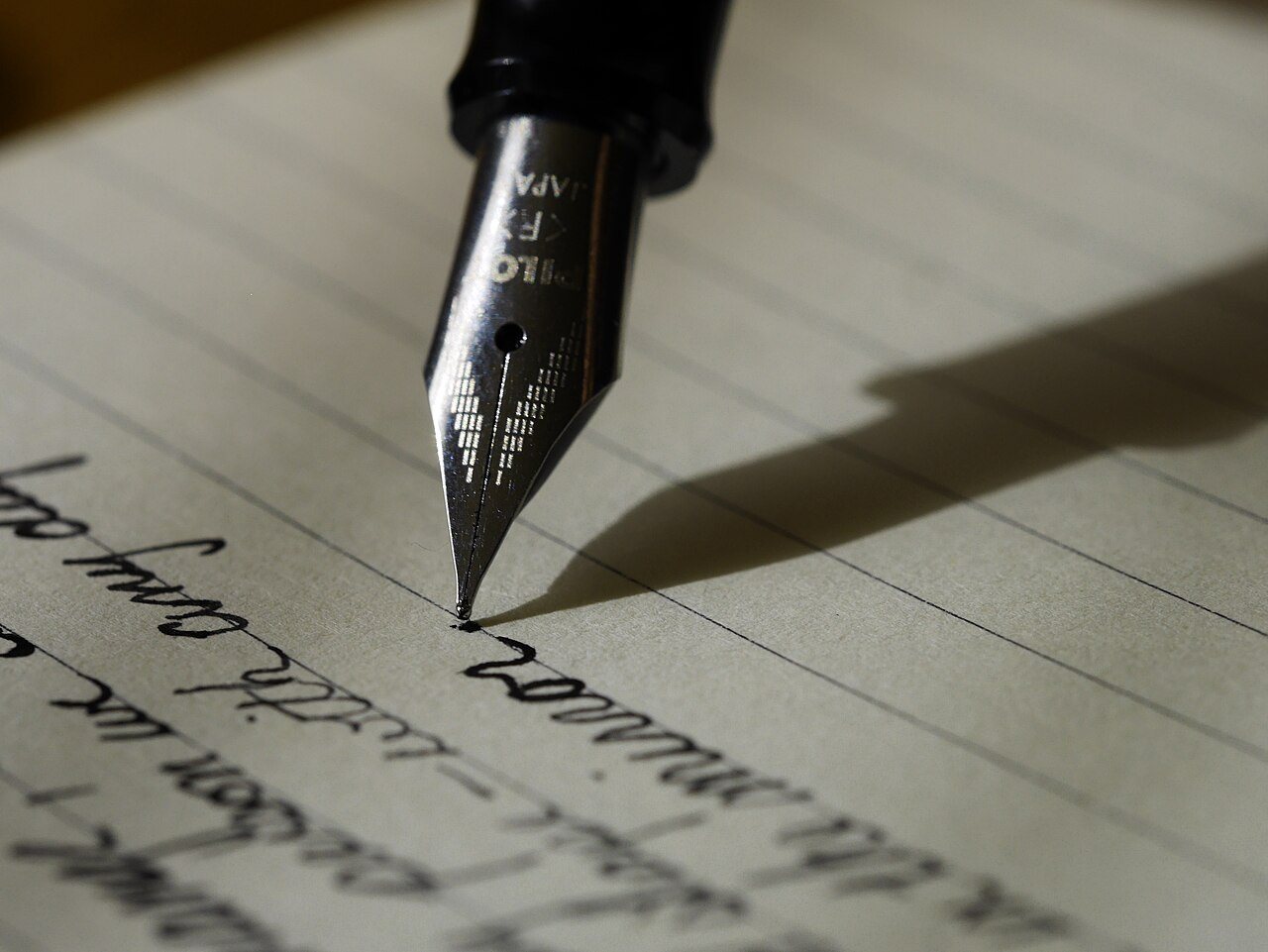 A fountain pen nib writing in cursive on lined paper