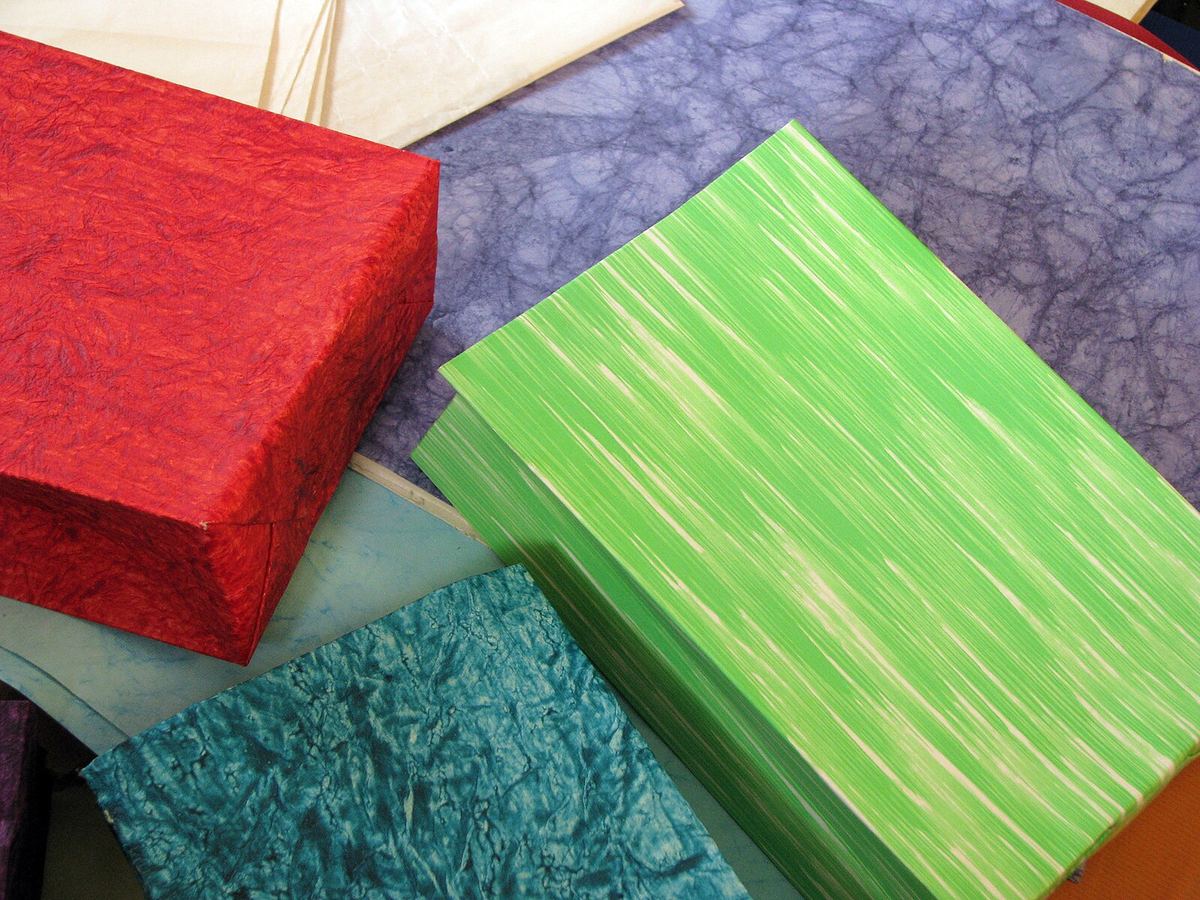 Handmade paper goods in red, green, teal and blue, with crinkled and streaked textures, made by a women's self-help group in India