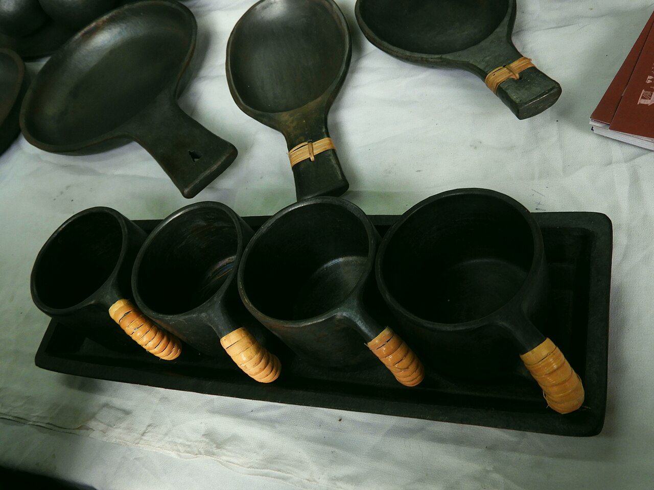 Black Longpi pottery pans and cups with cane-wrapped handles laid out on a cloth at a stall